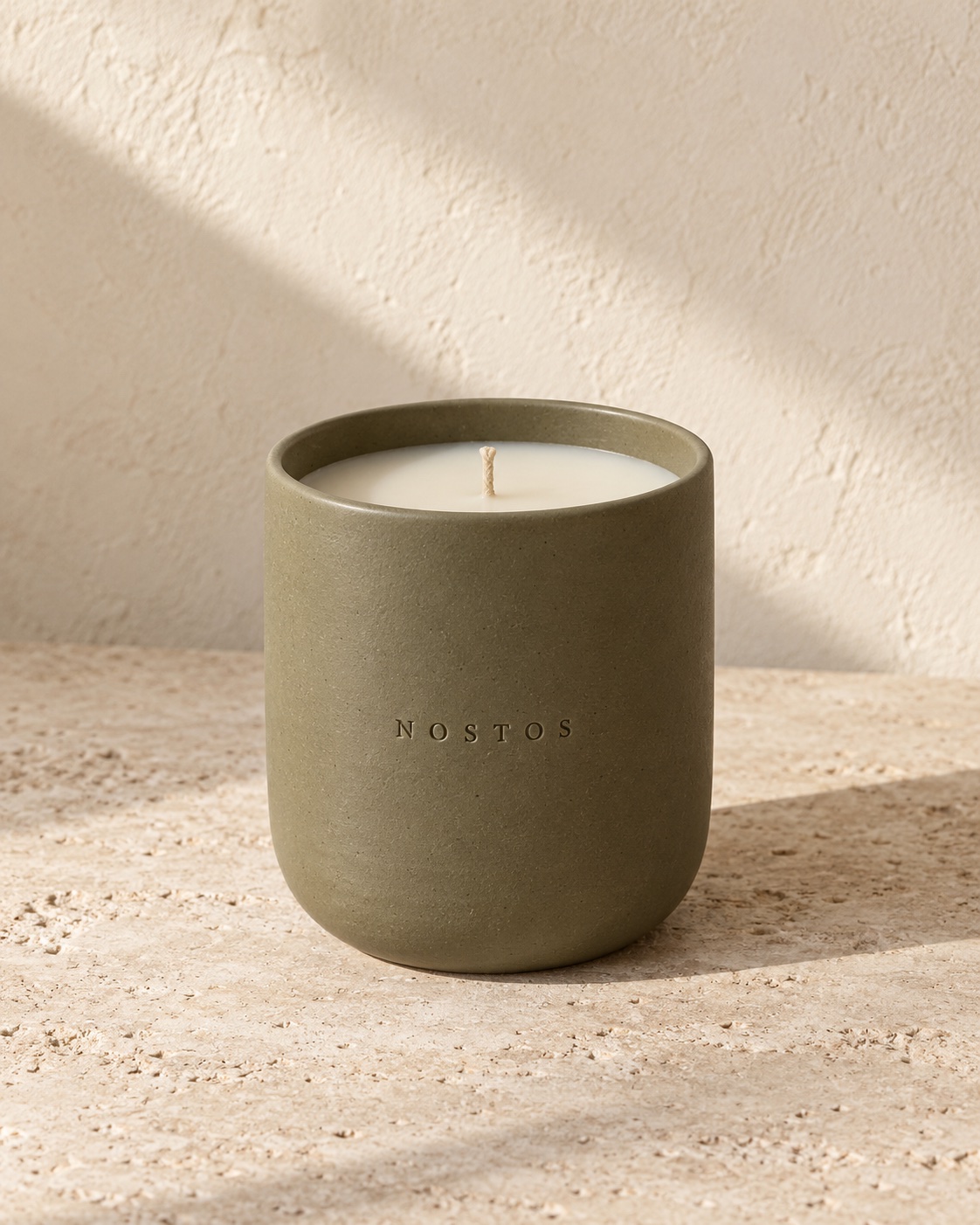 NOSTOS concept candle in a matte olive ceramic vessel on sunlit limestone.