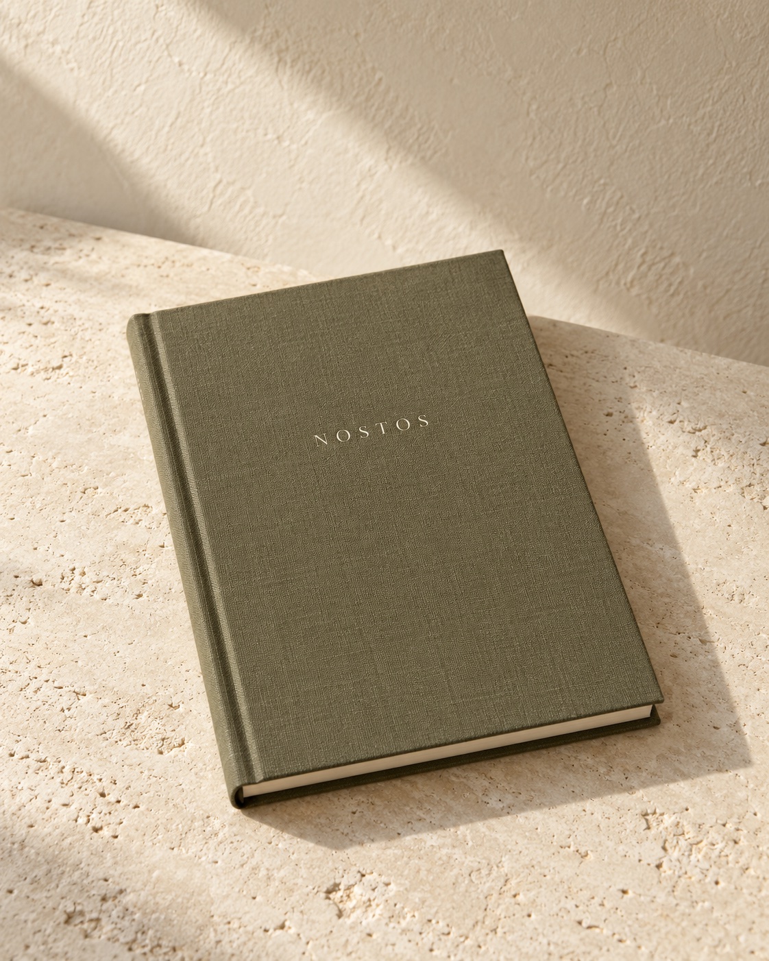 NOSTOS concept journal with an olive cloth cover, photographed on pale limestone.