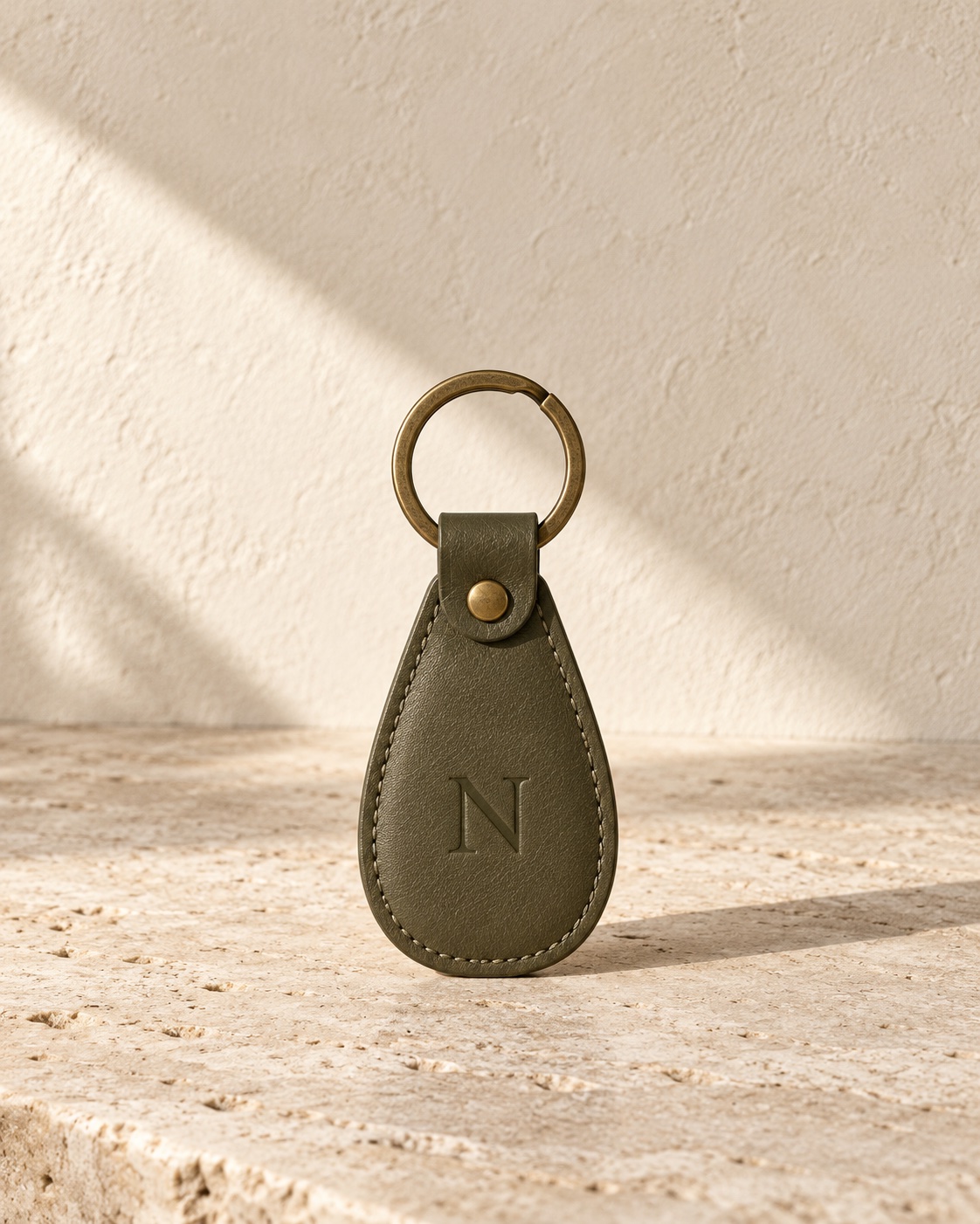 NOSTOS concept olive leather key tag with an embossed N and aged brass ring.