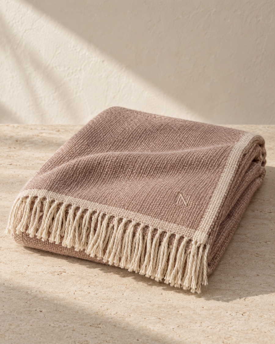 NOSTOS concept woven throw in soft rose, photographed on warm limestone.
